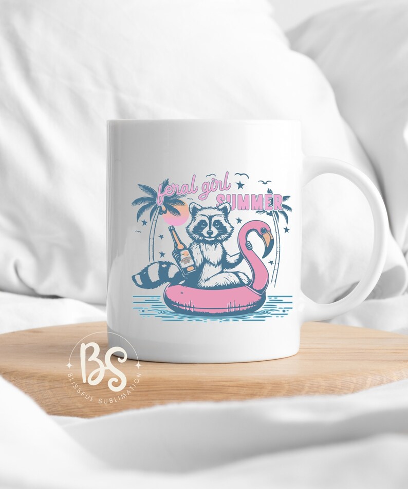 May include: White ceramic mug with a graphic of a raccoon wearing a pink flamingo float and holding a bottle of beer. The text "feral girl summer" is printed on the mug.
