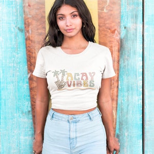 May include: A white t-shirt with a retro-style graphic that says "Vacay Vibes" in colorful letters. The graphic features palm trees and a peace sign.
