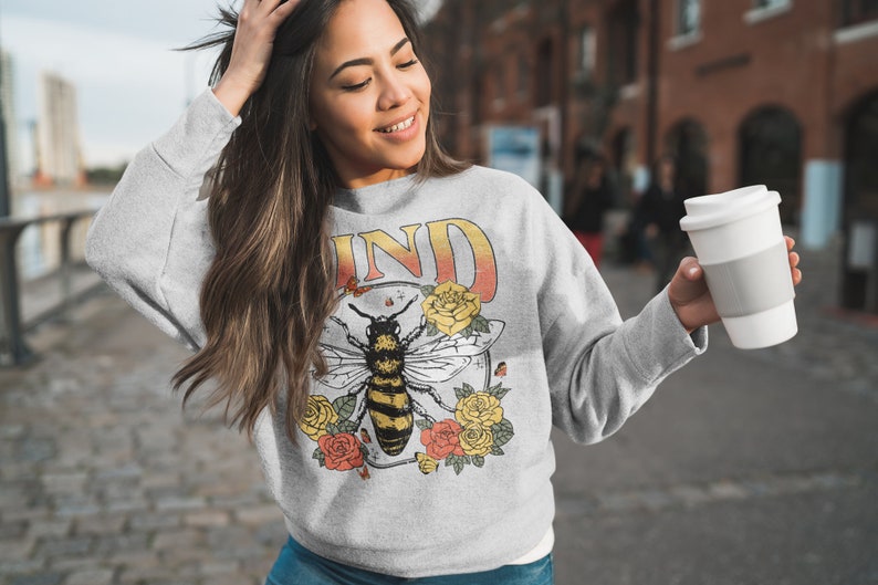May include: Gray sweatshirt with a bee and floral design. The text "KIND" is printed on the sweatshirt.