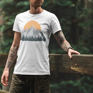 May include: White t-shirt with a graphic of a mountain range and a yellow sun. The graphic is in a vintage style with a blue and gray color scheme.