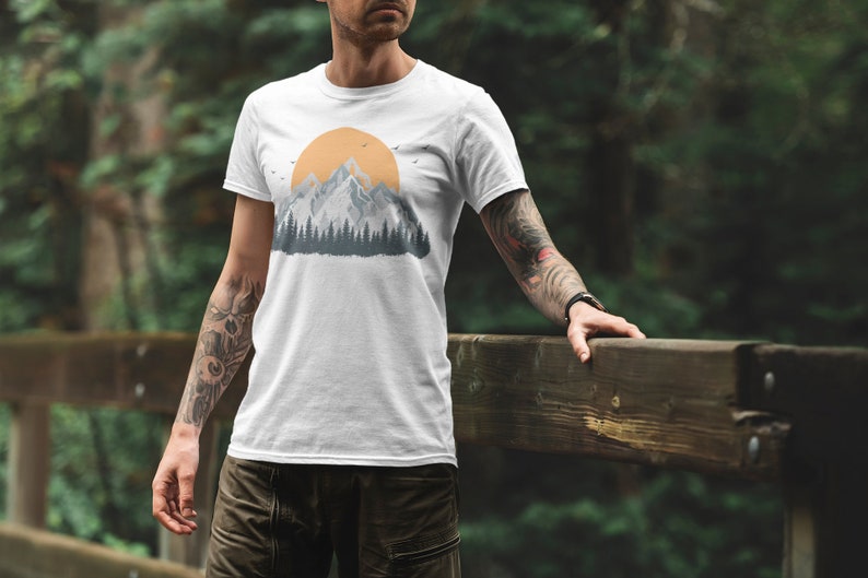 May include: White t-shirt with a graphic of a mountain range and a yellow sun. The graphic is in a vintage style with a blue and gray color scheme.