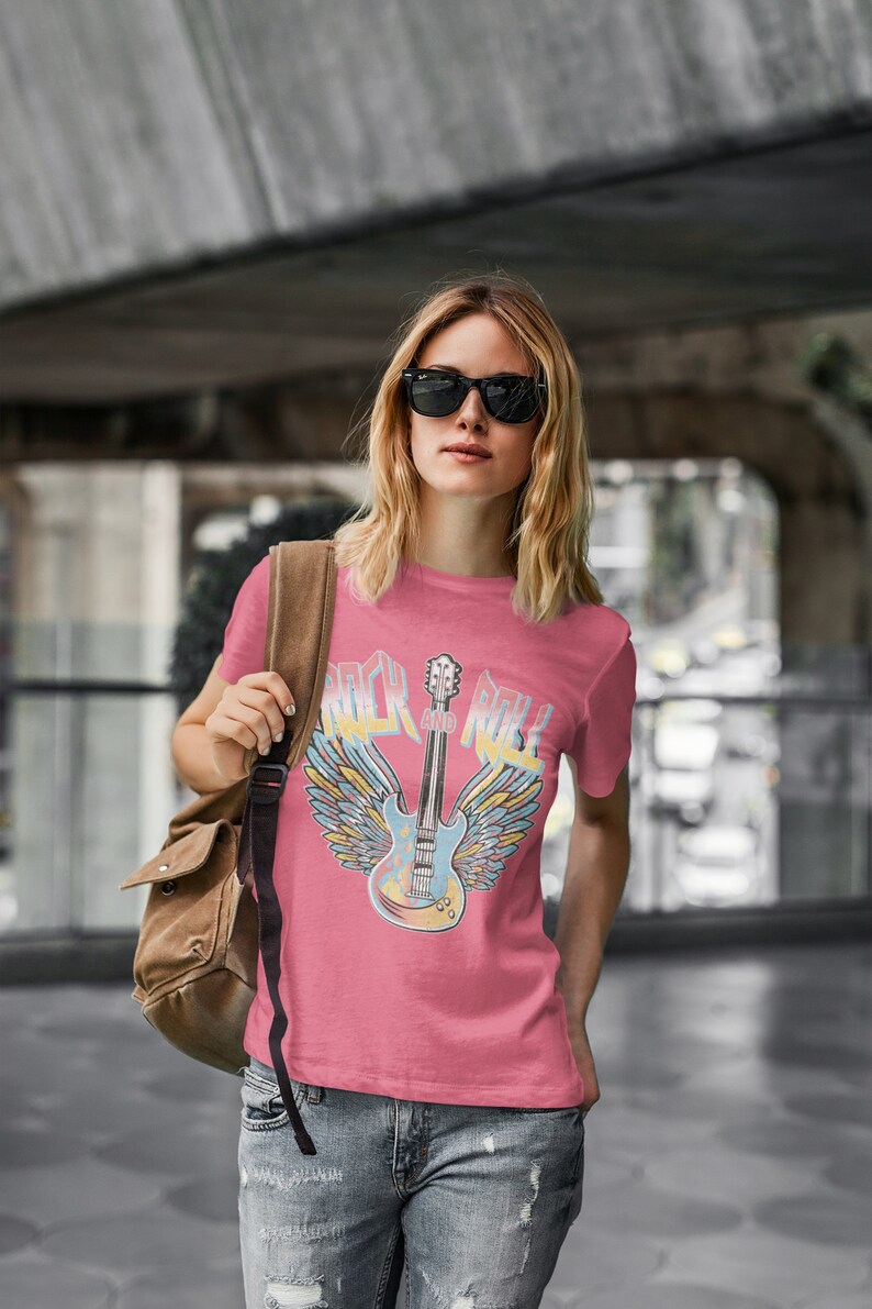 May include: A pink t-shirt featuring a graphic of a guitar with wings and the text "Rock and Roll".