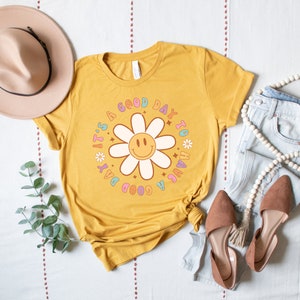 May include: A yellow t-shirt with a graphic of a daisy with a smiley face and the text "It's a good day to have a good day".