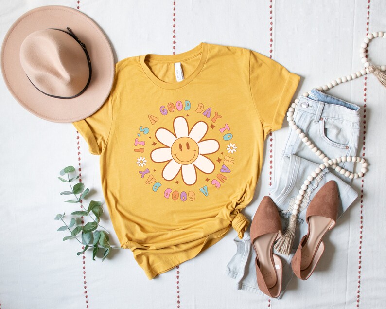 May include: A yellow t-shirt with a graphic of a daisy with a smiley face and the text "It's a good day to have a good day".