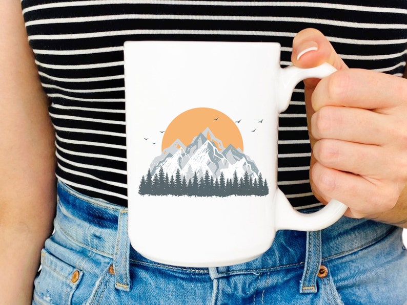 May include: White ceramic mug with a graphic of a mountain range with a sunset behind it. The mountains are gray and the sunset is orange.