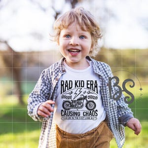 以下が含まれることがあります： 「Rad Kid Era Causing Chaos Life in the Fast Lane」というテキストと、黒いオートバイのグラフィックが描かれた白いTシャツ。