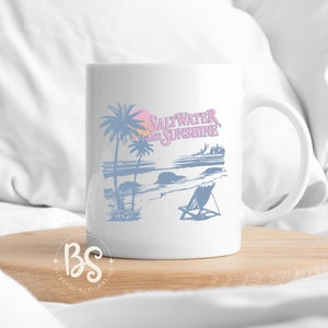 May include: White ceramic mug with a blue and pink design of palm trees, a beach scene, and the text "Saltwater and Sunshine".