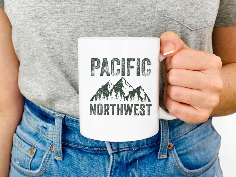 May include: White ceramic mug with a black and green graphic of mountains and trees. The text "PACIFIC NORTHWEST" is printed in black on the mug.