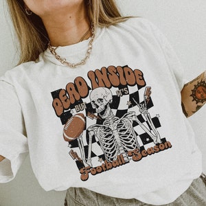 Puede incluir: Camiseta blanca con un gr&aacute;fico de un esqueleto sosteniendo un bal&oacute;n de f&uacute;tbol y el texto "Dead Inside But It's Football Season".