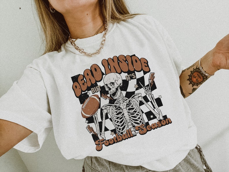 Puede incluir: Camiseta blanca con un gr&aacute;fico de un esqueleto sosteniendo un bal&oacute;n de f&uacute;tbol y el texto "Dead Inside But It's Football Season".