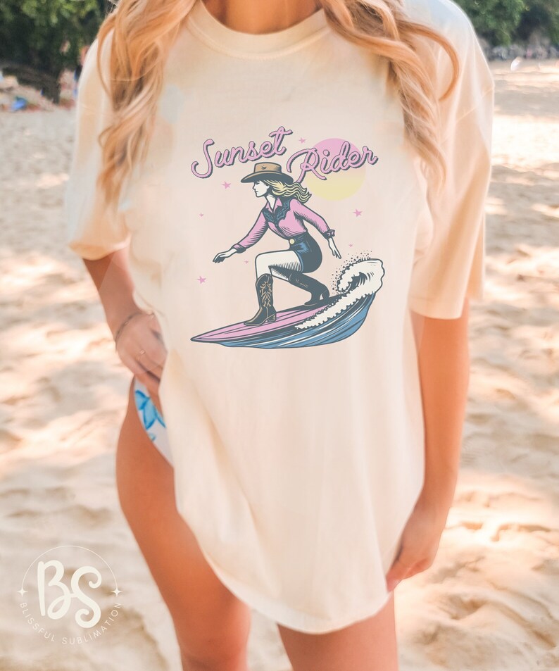Casual t-shirt with a Surfing Cowgirl print, featuring a cowgirl surfing a wave with the text "Sunset Rider," ideal for beachwear and casual outfits