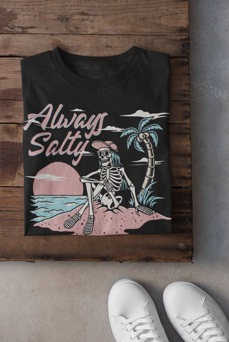 May include: Black t-shirt with a graphic of a skeleton wearing sunglasses and a hat sitting on a beach with a palm tree and the text "Always Salty".