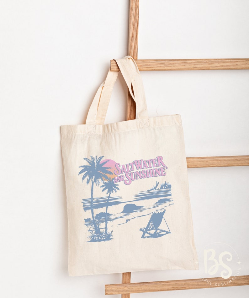 May include: A white canvas tote bag with a blue and pink graphic design of a beach scene with palm trees, a sunset, and a beach chair. The text "Saltwater and Sunshine" is printed on the bag.