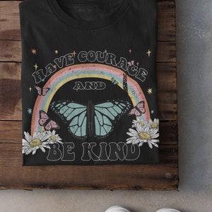 May include: Black t-shirt with a rainbow and butterfly graphic. The text "Have Courage and Be Kind" is printed on the shirt.