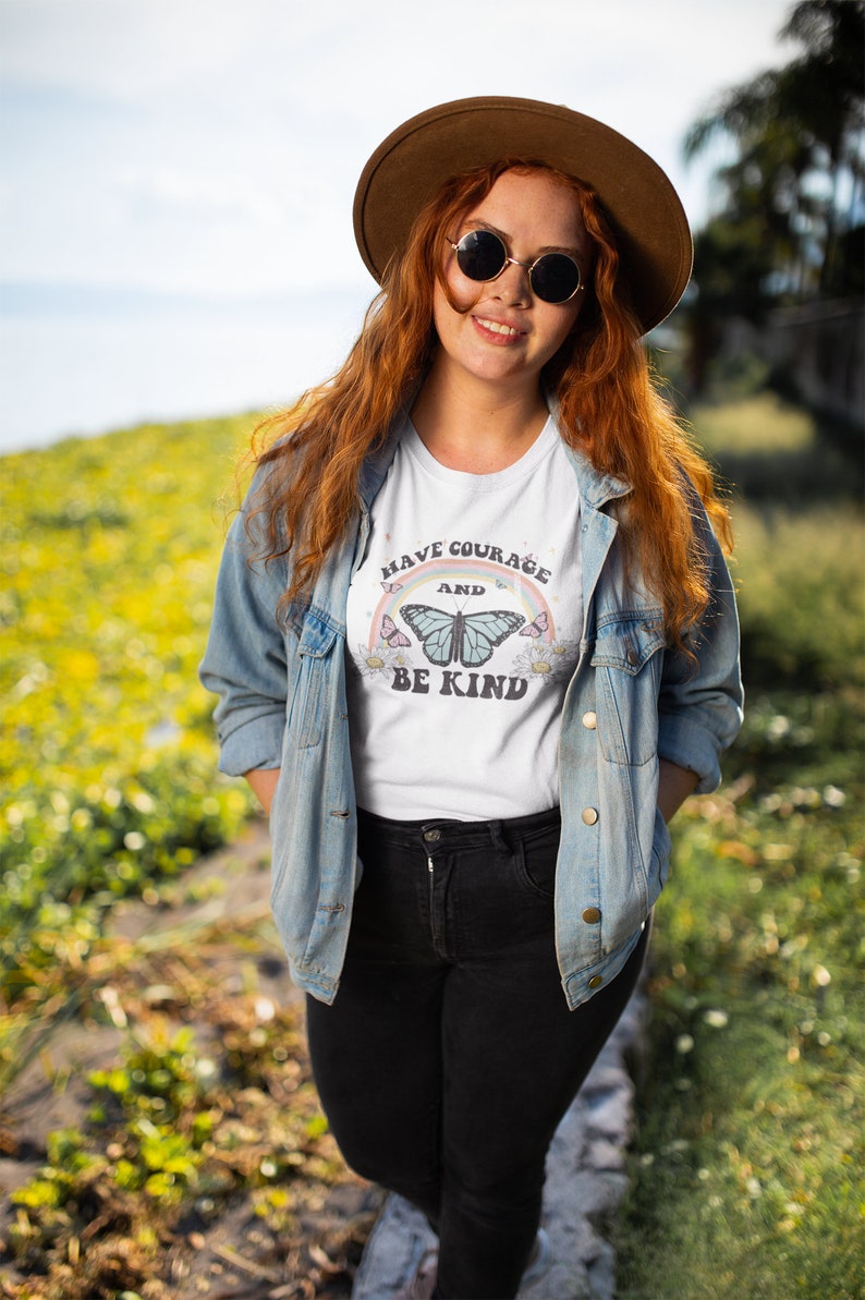 May include: A white t-shirt with a rainbow and butterfly graphic. The text on the shirt reads "Have Courage and Be Kind".