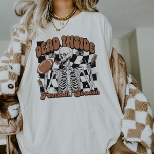 Puede incluir: Camiseta blanca con un gr&aacute;fico de un esqueleto sosteniendo un bal&oacute;n de f&uacute;tbol y el texto "Dead Inside But It's Football Season".