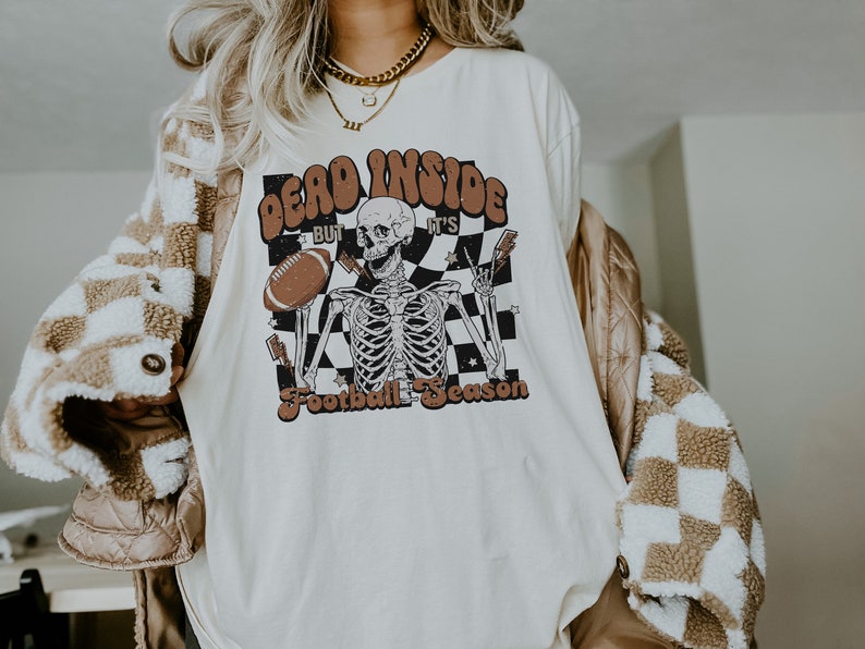 Puede incluir: Camiseta blanca con un gr&aacute;fico de un esqueleto sosteniendo un bal&oacute;n de f&uacute;tbol y el texto "Dead Inside But It's Football Season".