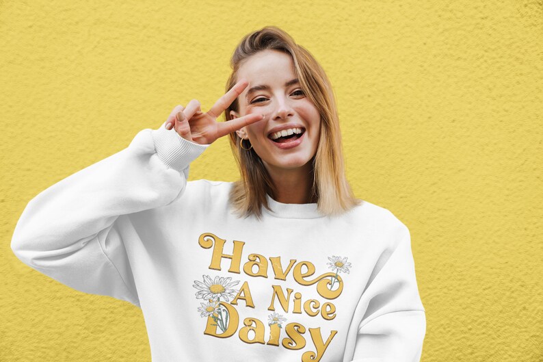 May include: White sweatshirt with a yellow graphic that says "Have A Nice Daisy" with daisy flowers.