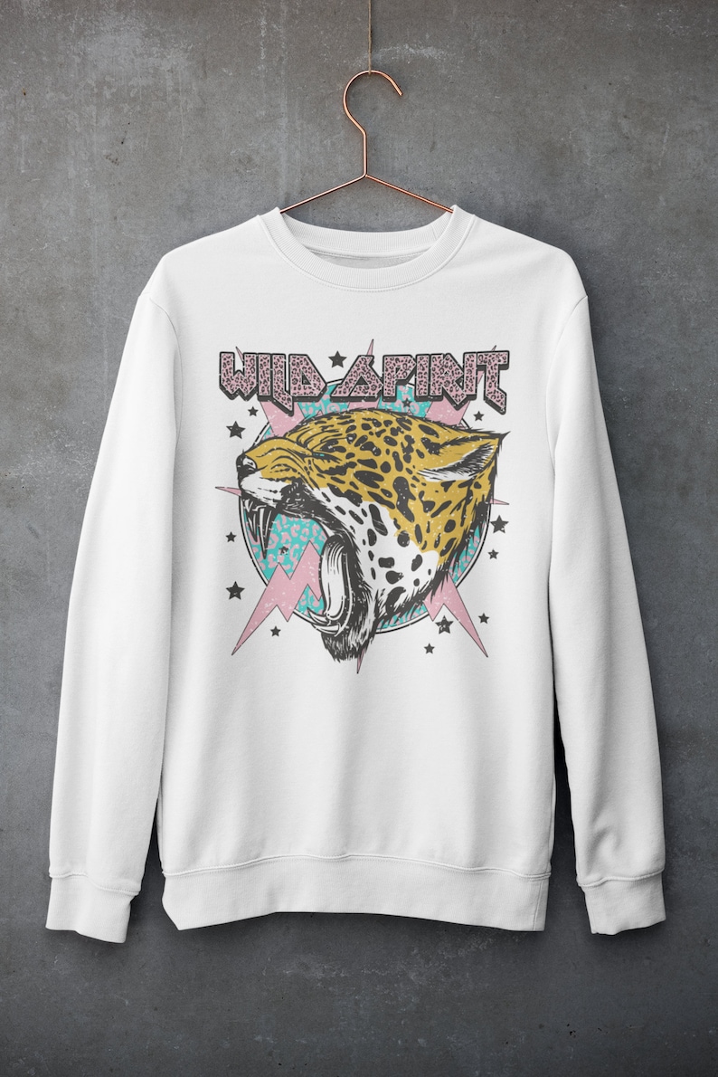 May include: White sweatshirt featuring a graphic print of a roaring jaguar head with a pink and blue background. The text "WILD SPIRIT" is above the jaguar head.