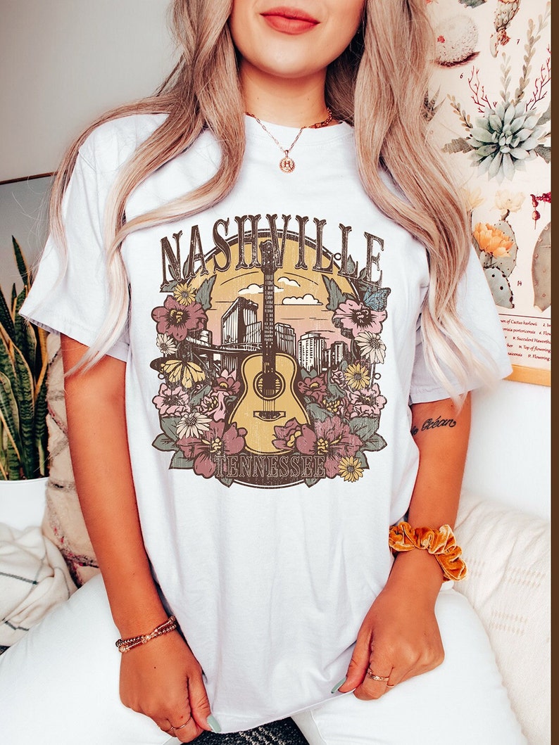 May include: White t-shirt with a graphic print of a guitar, flowers, and the text "Nashville Tennessee".