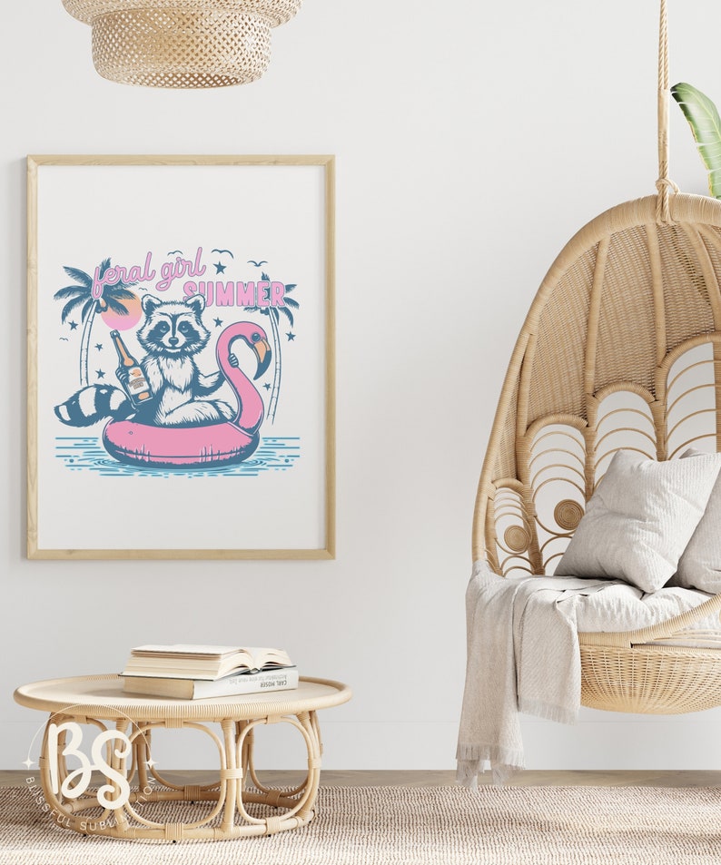 May include: A framed print with a cartoon raccoon wearing a life vest and holding a bottle of beer, floating on a pink flamingo pool float. The text "feral girl summer" is above the raccoon. The print is hanging on a white wall.