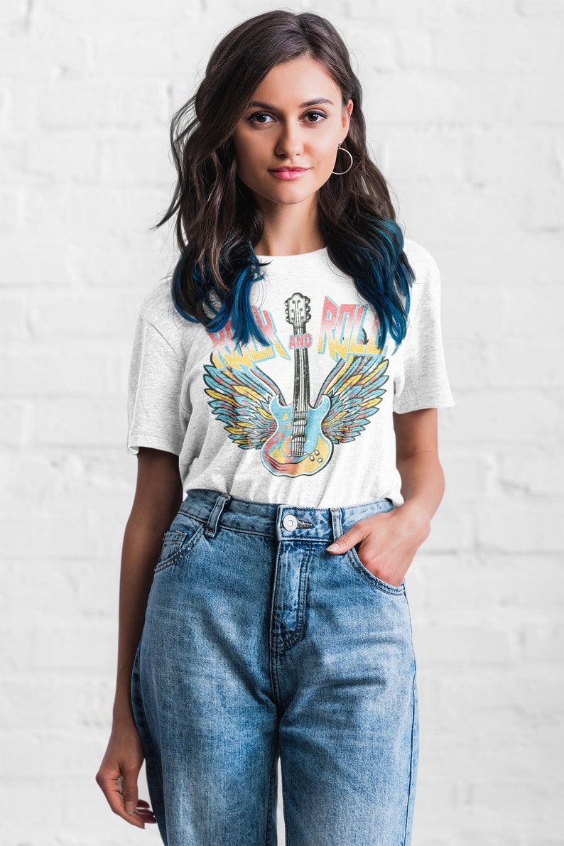 May include: A white t-shirt featuring a vintage-style graphic of a guitar with wings and the text "Rock and Roll".