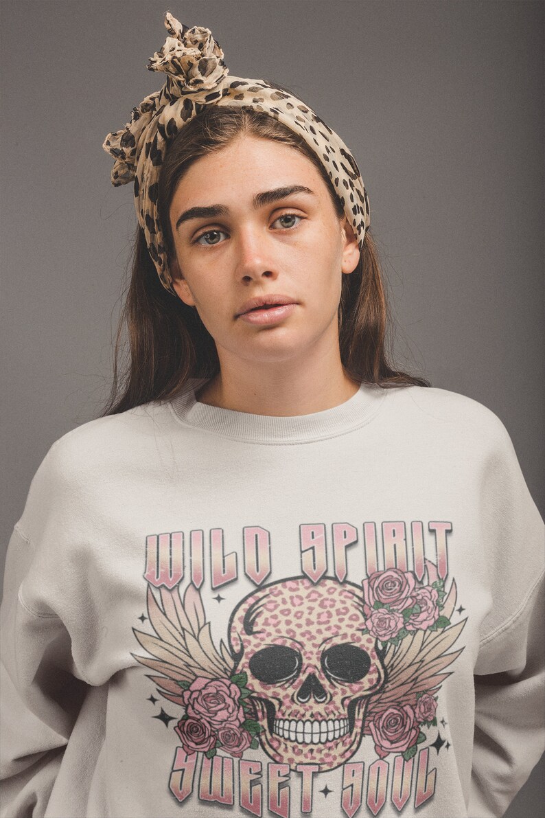 May include: A white sweatshirt with a pink and black skull graphic. The skull has a leopard print design and is surrounded by pink roses and wings. The text "WILD SPIRIT SWEET SOUL" is printed in pink on the sweatshirt.