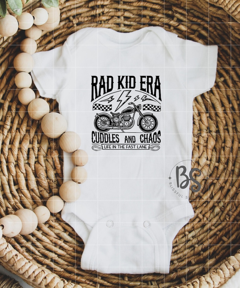 May include: White baby onesie with black text that reads "Rad Kid Era" with a lightning bolt and checkered flag design. Below the text is a black and white illustration of a motorcycle with the text "Cuddles and Chaos" and "Life in the Fast Lane".