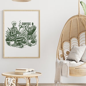 May include: A framed print with a green illustration of a skeleton sitting in a chair surrounded by plants and holding a cup of coffee. The text "Coffee & Plants" is written in green above the skeleton.