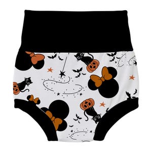 May include: White cotton baby bloomers with a black waistband and black trim. The bloomers feature a Halloween-themed print with black cats, pumpkins, stars, and Mickey Mouse ears with a bow.