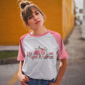 May include: A white and pink baseball tee shirt with a floral design and the word "LOVE" in a striped pattern.