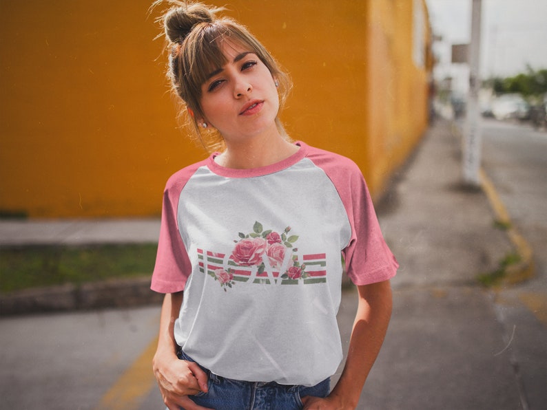 May include: A white and pink baseball tee shirt with a floral design and the word "LOVE" in a striped pattern.