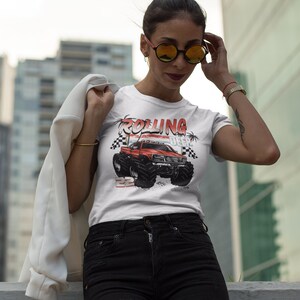 May include: White t-shirt with a red monster truck graphic and the text "Rolling Deep". The truck has black wheels and a red body. The t-shirt is worn by a person with black hair and sunglasses.