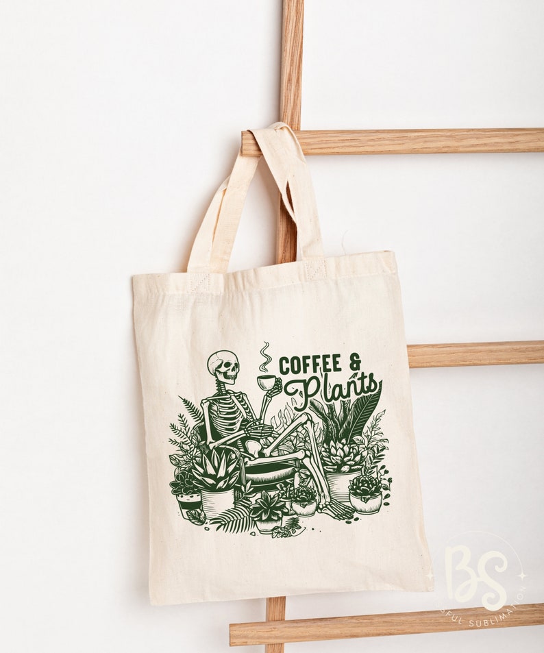 May include: A white tote bag with a green illustration of a skeleton sitting in a chair with a cup of coffee and surrounded by plants. The text "Coffee & Plants" is written in green above the skeleton.