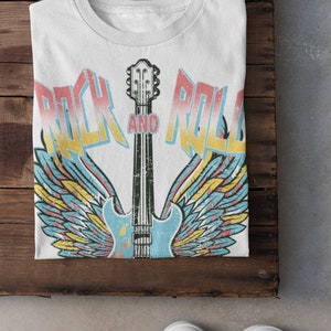 May include: White t-shirt featuring a vintage-style graphic of a guitar with wings and the text "Rock and Roll".