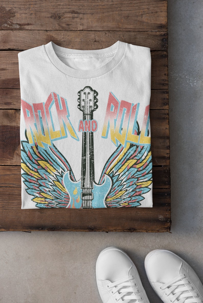 May include: White t-shirt featuring a vintage-style graphic of a guitar with wings and the text "Rock and Roll".