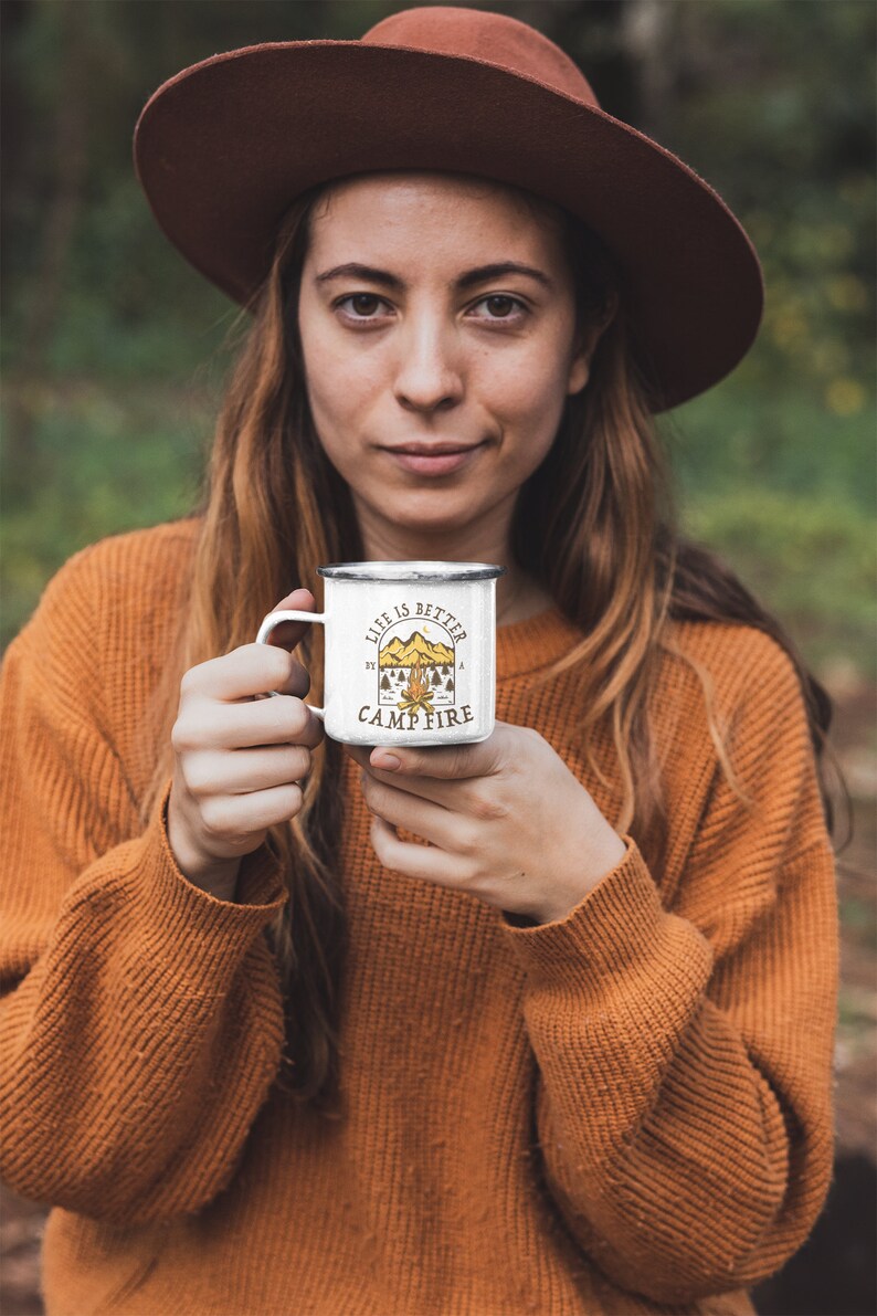 Pu&ograve; includere: Una tazza da campeggio in smalto bianco con manico nero e il testo "Life is better by a campfire" in lettere marroni e gialle. La tazza &egrave; decorata con una scena di fal&ograve; con montagne e alberi.