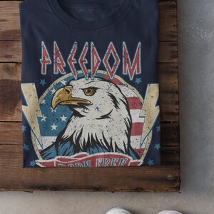 May include: A navy blue t-shirt with a distressed American flag design featuring a bald eagle and the words "FREEDOM BORN FREE".