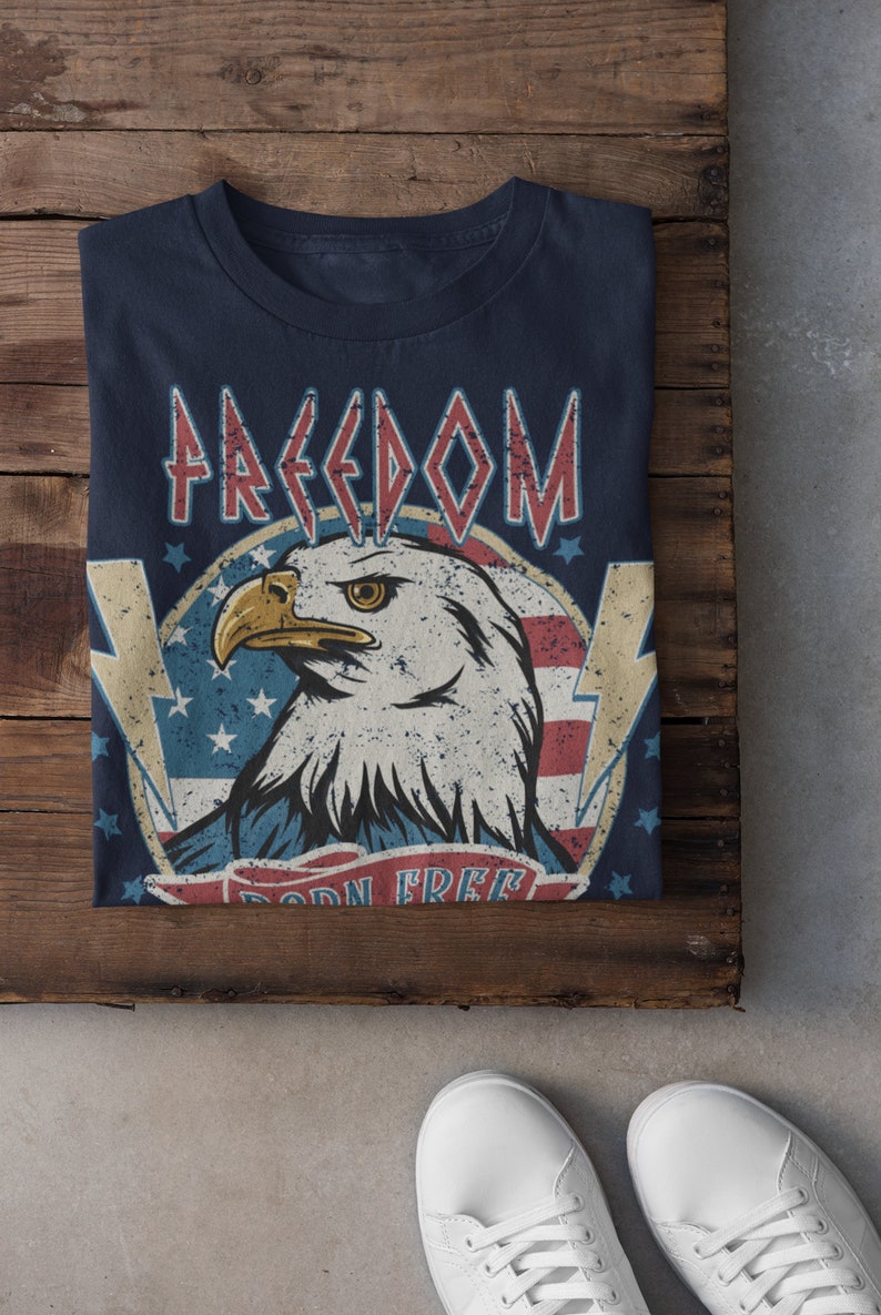 May include: A navy blue t-shirt with a distressed American flag design featuring a bald eagle and the words "FREEDOM BORN FREE".