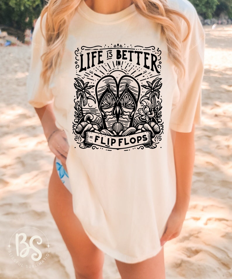 May include: A white t-shirt with a black graphic design that says "Life is better in flip flops". The graphic features a pair of flip flops with palm trees and waves.