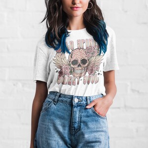 May include: White t-shirt with a graphic of a pink and black leopard print skull with wings and flowers. The text "Wild Spirit Sweet Soul" is printed below the skull.