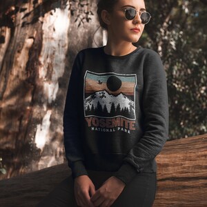 May include: A black sweatshirt featuring a vintage-style graphic of a mountain range and a sunset. The graphic includes the text "Yosemite National Park".