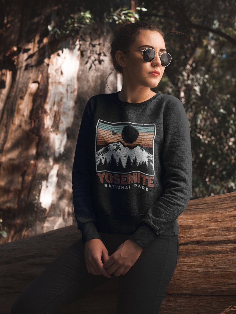 May include: A black sweatshirt featuring a vintage-style graphic of a mountain range and a sunset. The graphic includes the text "Yosemite National Park".