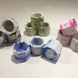 May include: A collection of nine small, hexagonal concrete planters in various colours, including black, white, green, pink, and blue. The planters have a marbled effect and are ideal for displaying small plants or succulents.