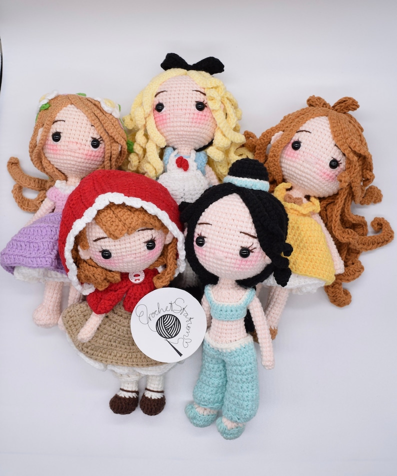 May include: Five crocheted dolls with different colored dresses and hair. The dolls are all smiling and have large eyes. The dolls are sitting on a white surface. The dolls are all wearing different outfits. The dolls are all handmade. The dolls are all unique. The dolls are all beautiful. The dolls are all perfect for a child's playroom. The dolls are all perfect for a collector. The dolls are all perfect for a gift. The dolls are all perfect for a special occasion.