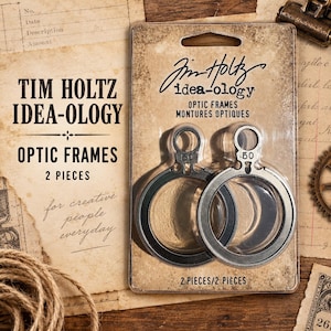 May include: Two circular metal optic frames by Tim Holtz idea-ology packaged in a clear plastic blister pack on a tan cardboard backing. Each frame features a small circular loop at the top with the number .50 printed on the metal surface.