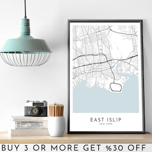 Puede incluir: Impresión de mapa en blanco y negro de East Islip, Nueva York, con fondo azul claro. La impresión está enmarcada en un marco negro y se muestra en un estante con una cámara, lápices y libros.