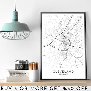 Puede incluir: Impresión en blanco y negro de un mapa de Cleveland, Tennessee en un marco negro. La impresión está en un estante con una cámara, lápices y libros. El texto "BUY 3 OR MORE GET %30 OFF" está en el estante debajo de la impresión.