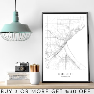 Pode incluir: Impressão em preto e branco de uma arte de linha de um mapa de Duluth, Minnesota. A impressão é emoldurada em uma moldura preta e está pendurada em uma parede branca. O texto "DULUTH" e "MINNESOTA" é impresso abaixo do mapa.