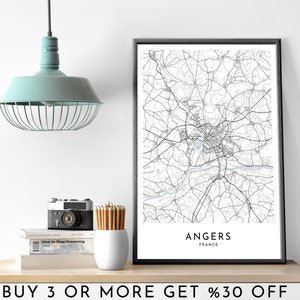 May include: Black and white line art map print of Angers, France in a black frame. The print is on a white background and has the city name and country printed below the map. The print is on a shelf with a camera, pencils, and books.